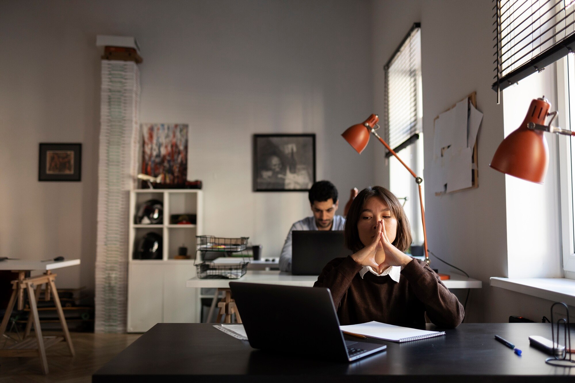 Two coworkers sit quietly at separate desks in a dim office, a visual cue of disengaged, low-energy workplaces in 2026.