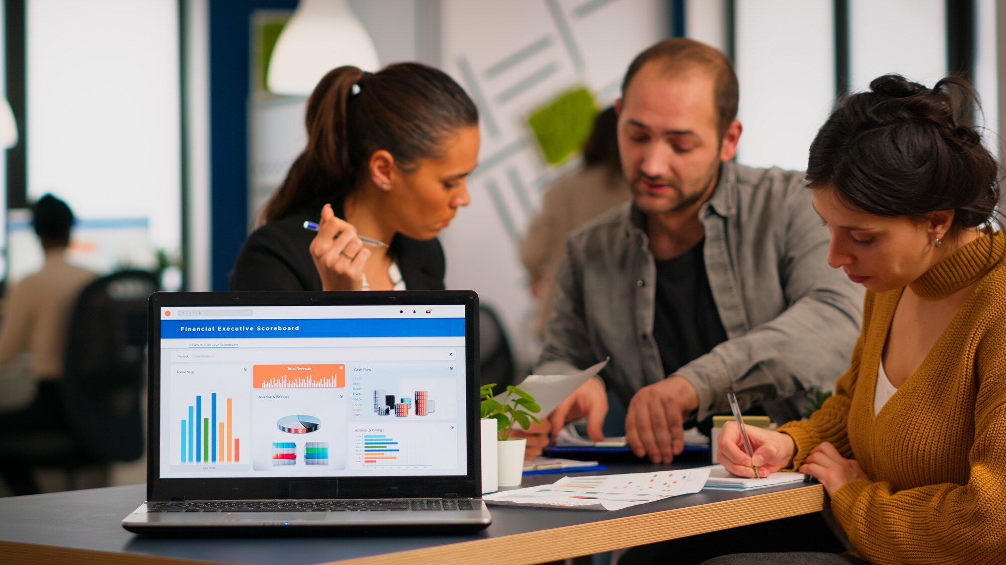 A diverse team reviewing a financial dashboard on a laptop in a co-working space, a visual of cross-functional people analytics in practice