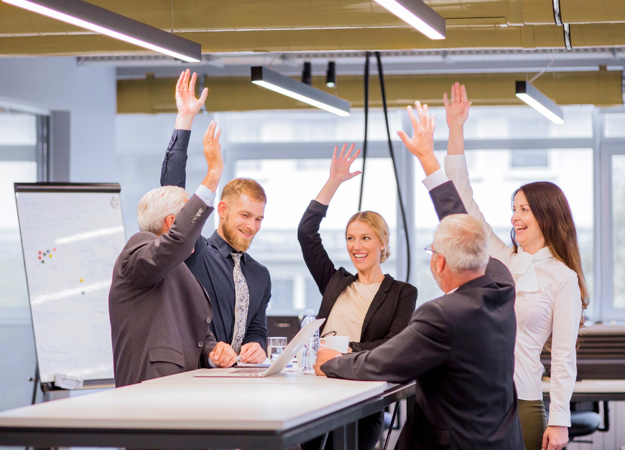 Team members raising hands in a meeting room, representing positive employee satisfaction survey results